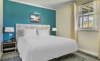 a modern bedroom with blue walls , white bedding , and two white pillows on the bed , along with a window and a nightstand at The Kenmore Club