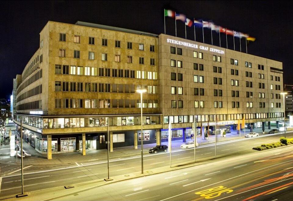 a large building with multiple flags flying in front of it , illuminated at night at Steigenberger Graf Zeppelin