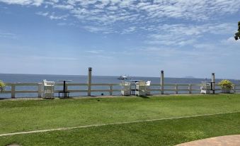 a grassy field with two white chairs and a wooden fence overlooking the ocean , creating a picturesque scene at Sierra Resort