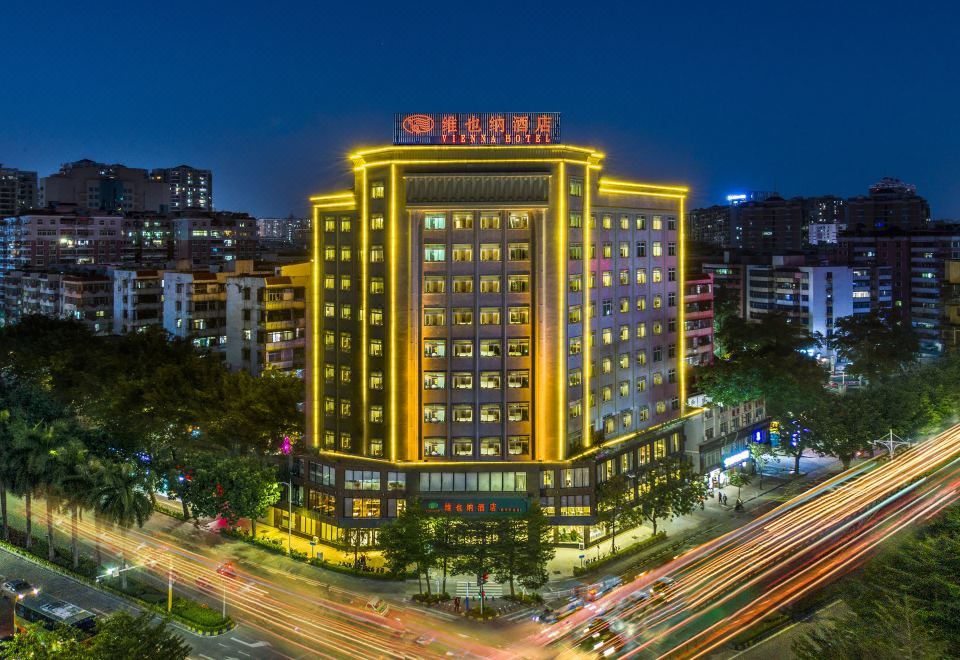 a large , illuminated building with a red sign in chinese characters is surrounded by other buildings and traffic on the street at Vienna Hotel