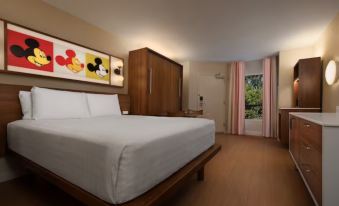 a large bed with white sheets and a wooden headboard is in a room with pink curtains at Disney's Pop Century Resort - Classic Years