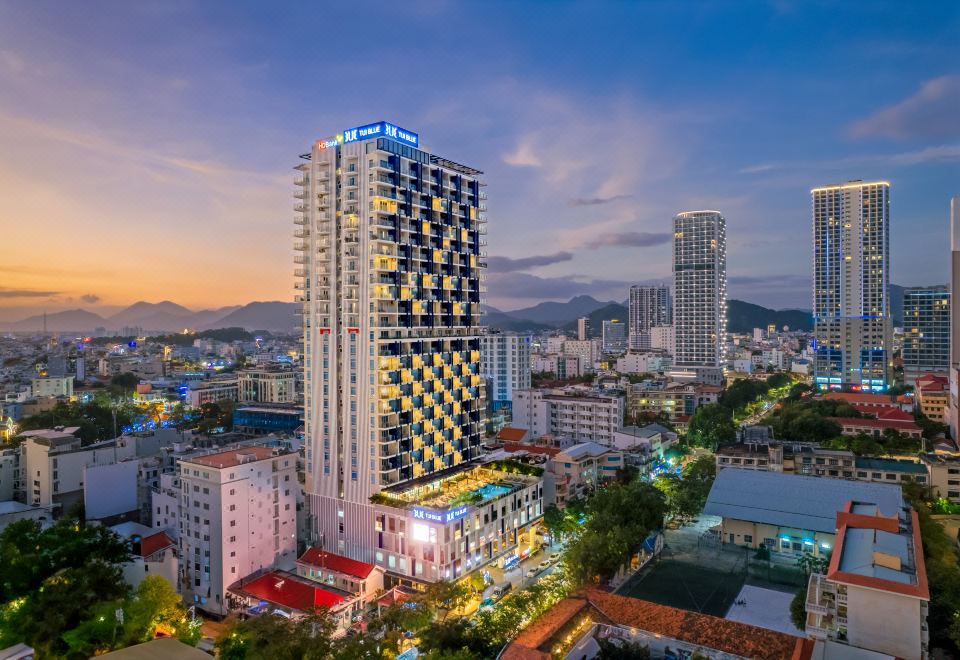 a cityscape with a tall hotel building illuminated at night , surrounded by other buildings and skyscrapers at TUI BLUE Nha Trang