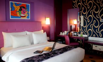 a hotel room with a purple bed , a laptop on the bedside table , and a chair in the corner at Aquarius Boutique Hotel Sampit