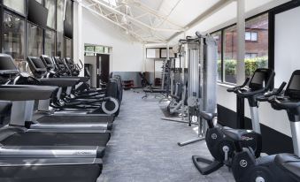 a well - equipped gym with various exercise equipment , including treadmills and stationary bikes , under a large skylight at Delta Hotels Waltham Abbey