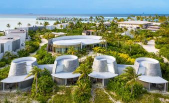 aerial view of a modern beach resort surrounded by palm trees , with multiple buildings and umbrellas visible at Hard Rock Hotel Maldives - Complimentary Roundtrip Speed Boat Transfer Until 31st October 2025