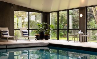 a modern indoor swimming pool with large windows , surrounded by chairs and potted plants , creating a relaxing atmosphere at Sudima Auckland Airport