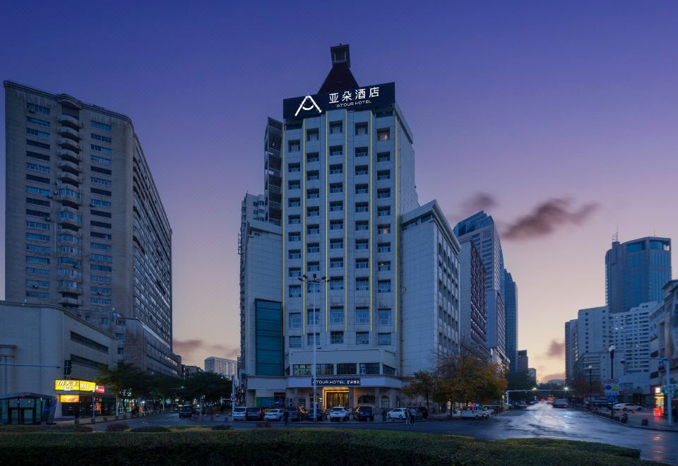 a modern city skyline with multiple tall buildings , including a hotel and office buildings , set against a backdrop of a blue sky at dusk at Atour Hotel