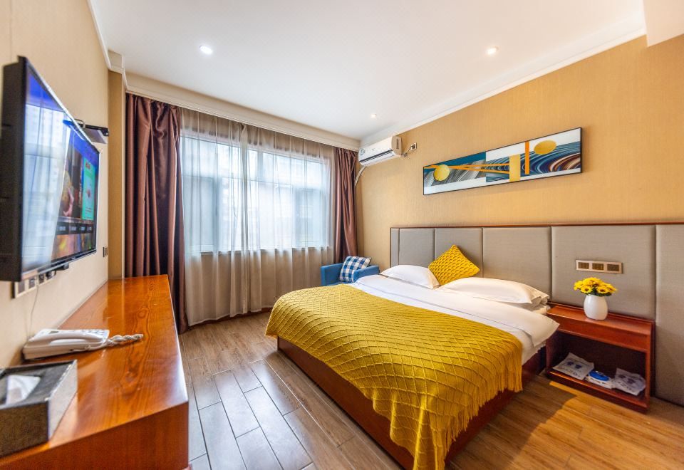 a well - lit bedroom with a large bed , wooden flooring , and curtains , as well as a desk area at Good Hotel (Beijing East Road Gaoxin Avenue Subway Station)