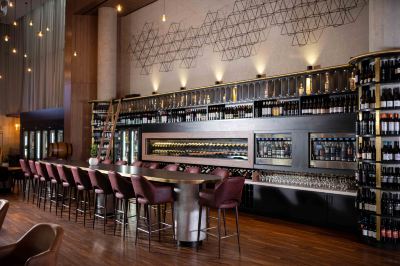 a modern bar with a long counter and several stools , as well as a variety of bottles and wine glasses at Oval Hotel at Adelaide Oval, an EVT hotel