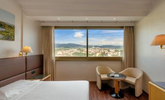 a hotel room with a large window overlooking a cityscape , featuring a bed , chair , and table at Hotel Minerva