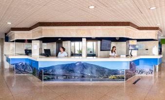 a reception area with two people at the counter , a large mural of a mountain on the wall at Catalonia Punta del Rey