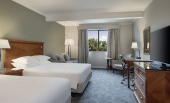 a modern hotel room with two beds , nightstands , and a view of trees outside the window at Delta Hotels Waltham Abbey