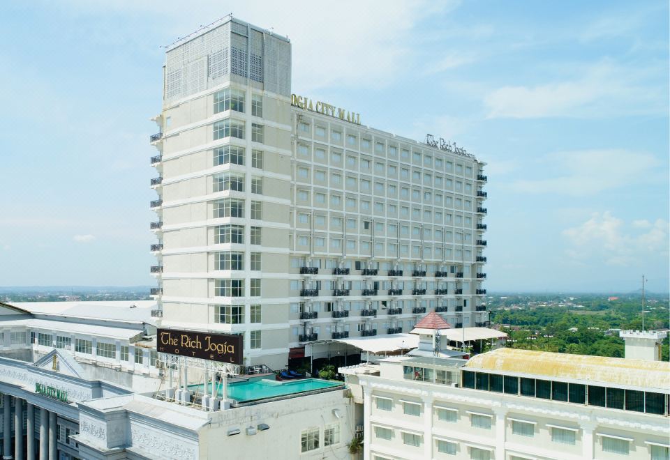 "a tall white building with a sign that reads "" parque hotel "" is surrounded by other buildings" at The Rich Jogja Hotel