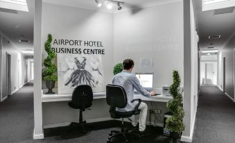 a man sitting at a desk in an airport hotel business center , working on a computer at Airport Hotel Sydney