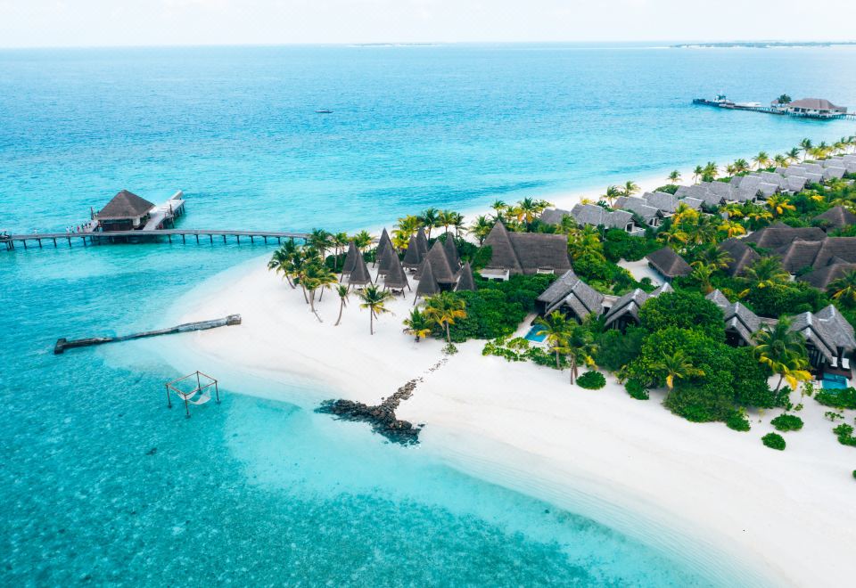 a tropical island with white sand , turquoise water , and thatched - roof buildings , as well as a bridge connecting to the mainland at Heritance Aarah-Premium All Inclusive