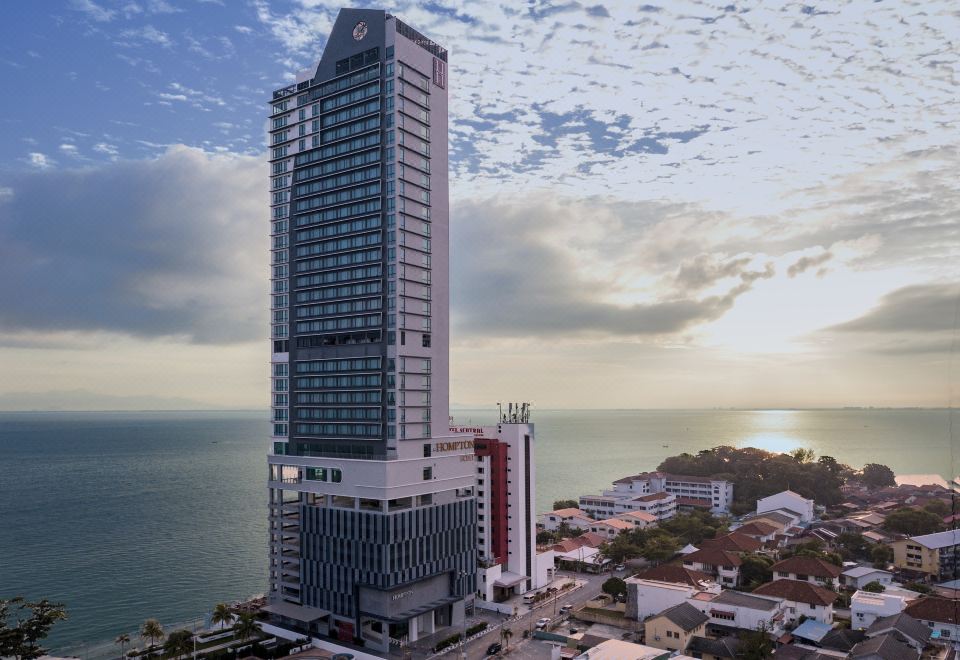 a large , modern skyscraper with a swimming pool in front of it , situated near the ocean at Hompton Hotel by The Beach