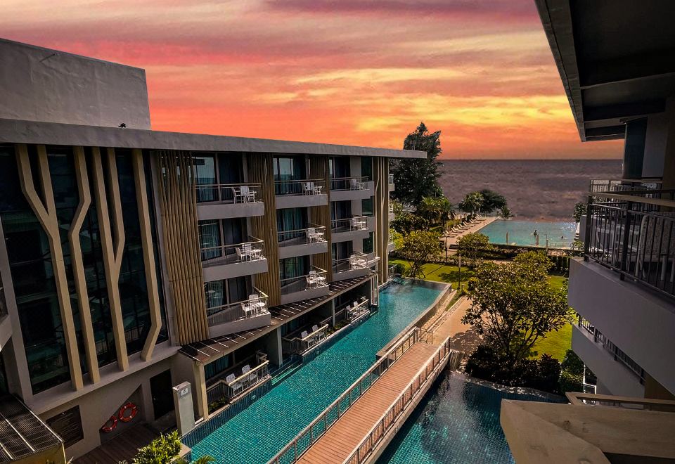 a resort with a large pool surrounded by multiple buildings and a beautiful sunset in the background at Sand Dunes Chaolao Beach Resort