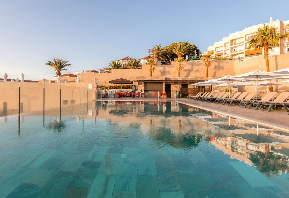 a large outdoor pool surrounded by lounge chairs and umbrellas , providing a relaxing atmosphere for guests at Catalonia Punta del Rey
