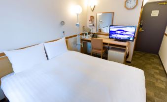 a hotel room with a white bed , a tv on a desk , and a clock on the wall at Toyoko Inn Oita Ekimae