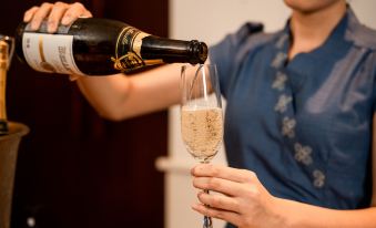 a woman is pouring champagne into a wine glass , standing in front of a dining table at Salinda Resort Phu Quoc - Sparkling Wine Breakfast