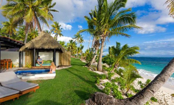 a woman sitting on a lawn with a thatched - roof hut in the background , overlooking the ocean at Matamanoa Island Resort