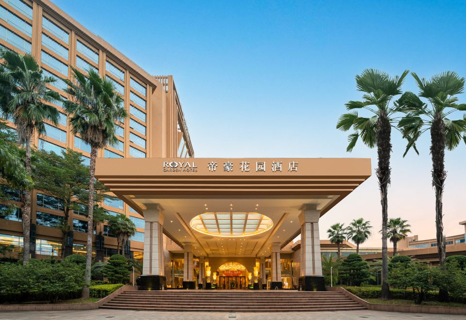 the entrance of a large hotel with a large sign above the doorway , surrounded by palm trees at Royal Garden Hotel