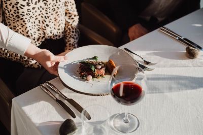 a woman is sitting at a table with a plate of food , wine glass , and knife at Oval Hotel at Adelaide Oval, an EVT hotel