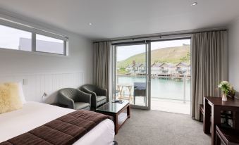 a hotel room with a large bed , two chairs , and a view of the water through a sliding glass door at Marsden Lake Resort Central Otago