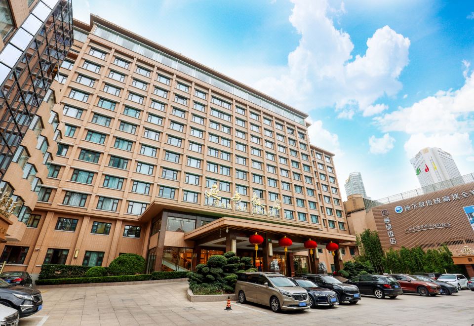 The front entrance of a hotel in an urban area features a spacious parking lot and a stone walkway at Yan An Hotel