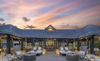 a modern , minimalist restaurant with wooden floors and large windows , surrounded by comfortable seating and outdoor dining areas at Naladhu Private Island