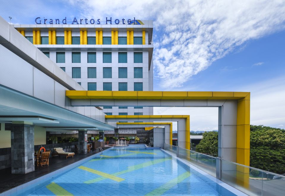 a modern hotel with a swimming pool and yellow columns , under a clear blue sky at Grand Artos Hotel & Convention