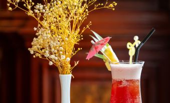a table with a tall glass of red drink , surrounded by various decorative items such as vases , flowers , and candles at Lbn Asian Hotel