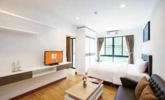 a modern living room with a bed , tv , and window , along with wooden flooring and white walls at B2 Sriracha Premier Hotel