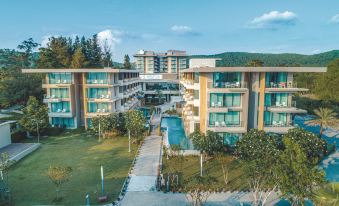 a large , modern hotel building with multiple stories and balconies , surrounded by lush greenery and clear blue skies at Sand Dunes Chaolao Beach Resort