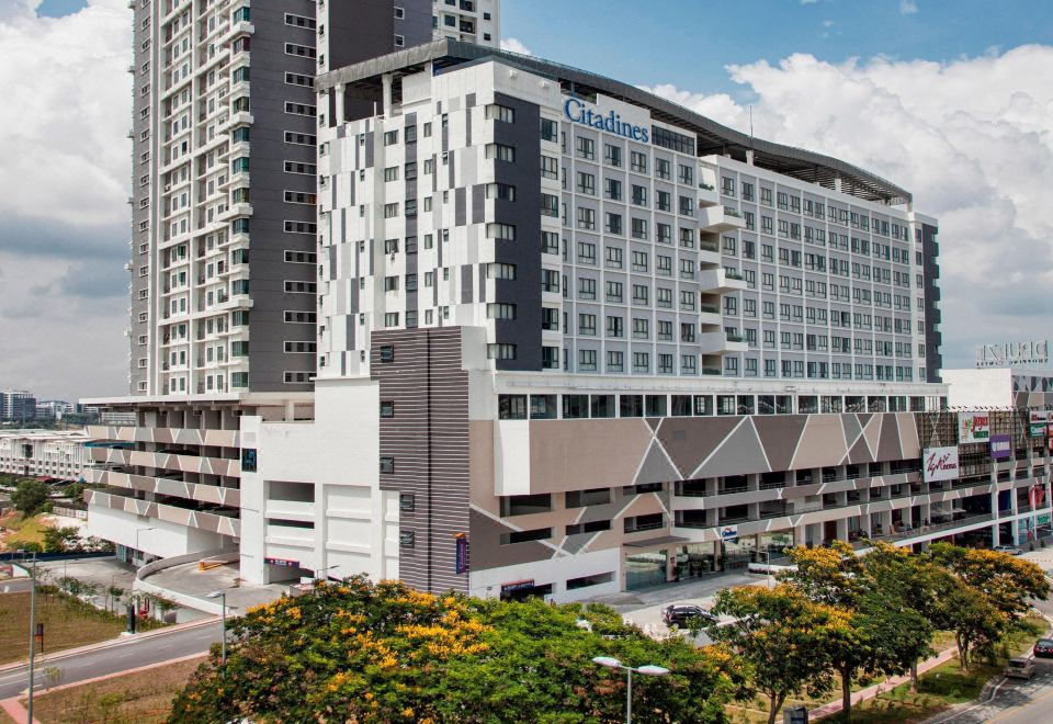 a modern apartment building with a parking garage and trees in the foreground , under a clear blue sky at Citadines DPulze Cyberjaya