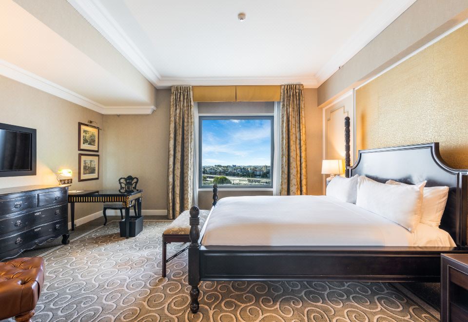 a luxurious hotel room with a large window offering a view of the city , a black bed , and a desk at Stamford Plaza Brisbane