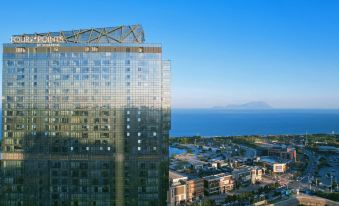 A large building with many windows is seen, along with an adjacent skyscraper in the middle at Four Points by Sheraton Qingdao, West Coast