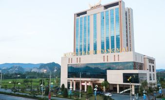 "a large building with a gold and white sign that says "" hotel bangkok "" is surrounded by trees and mountains" at Muong Thanh Grand Hoang Mai - Nghe An