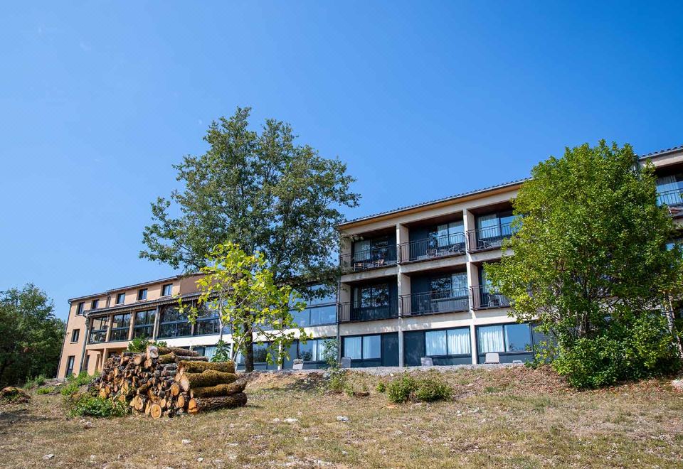 a modern , multi - story building with wooden accents and large windows , situated on a hillside with trees and logs at Le Bois d'Imbert