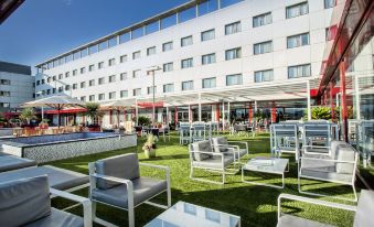a modern hotel with a large outdoor patio area , surrounded by lush greenery and clear blue skies at Alexandre Hotel Frontair Congress