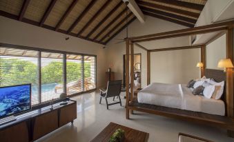 a large bedroom with a four - poster bed , wooden furniture , and a view of a pool outside at The Residence Maldives at Dhigurah