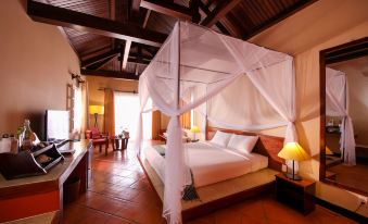 a luxurious bedroom with a large bed and a canopy , surrounded by wooden furniture and red tile flooring at Victoria Nui Sam Lodge