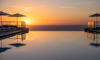 a serene pool with a covered seating area and a clear horizon , set against the backdrop of a beautiful sunset at Jumeirah Port Soller Hotel and Spa