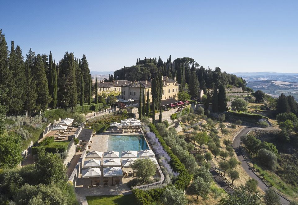 aerial view of a resort with a large pool surrounded by lounge chairs and umbrellas , surrounded by trees at Rosewood Castiglion del Bosco