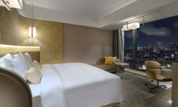 a luxurious hotel room with a white bed , a couch , and a window overlooking the city at Caesar Park Hotel Banqiao