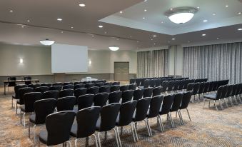 a conference room with rows of black chairs and a projector screen at the front at Delta Hotels Waltham Abbey
