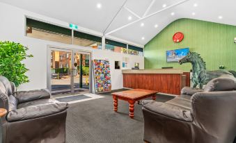 a hotel lobby with a wooden reception desk , two leather chairs , and a couch arranged in front of it at APX Parramatta