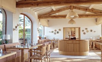 a modern , minimalist restaurant interior with wooden beams and white walls , featuring multiple dining tables and chairs , as well as a bar area at Capelongue, a Beaumier Hotel & Spa