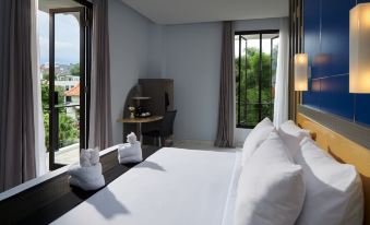 a large bed with white linens is in a room with a desk and window at El Hotel Malang