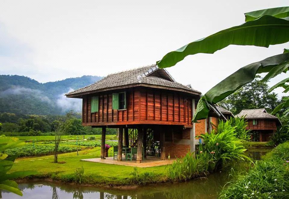 a wooden house with a green roof is situated on stilts over a small body of water at Lhongkhao Samoeng by Chi Villa